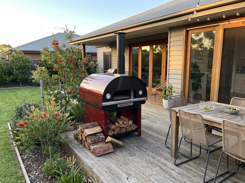 Marchiceiu wood-fired pizza oven set up on an outdoor deck with firewood stacked beside it