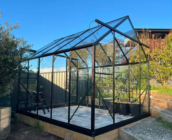 A customer's finished Wintergardenz 8ft Wide Glasshouse in their backyard, surrounded by raised garden beds