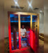 Person sitting in an infrared sauna with a red light therapy panel glowing beside them